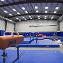 Large gymnasium with blue mats, bars. balance beams and a pommel horse.