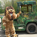 Lion mascot waving in front of a jungle-painted train.