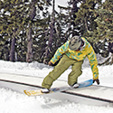 Brightly clothed snowboarder rides a flat box terrain park feature.