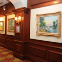 Hallway of gold framed paintings of landscapes.